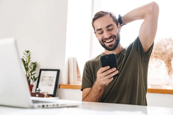 Image of handsome laughing man typing on laptop and using cellphone — Stock Photo, Image