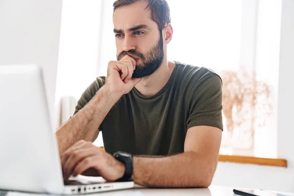 Bild eines gutaussehenden, konzentrierten Mannes, der im Sitzen auf dem Laptop tippt — Stockfoto