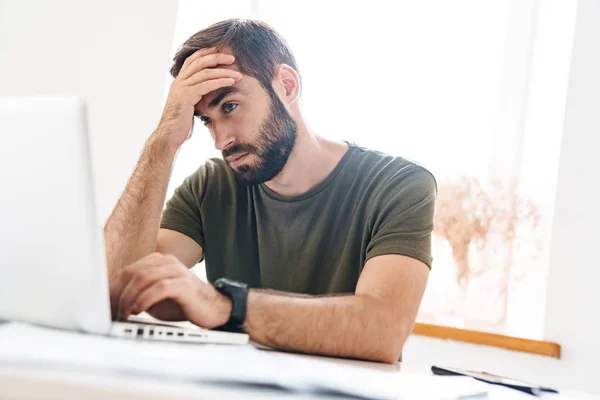 Imagen del hombre concentrado guapo escribiendo en el ordenador portátil mientras está sentado —  Fotos de Stock