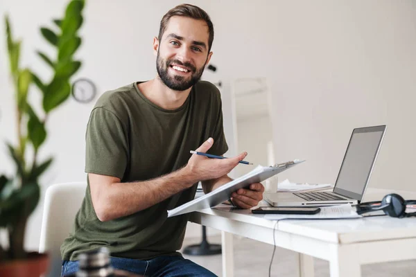 Bild eines lächelnden jungen Mannes, der in die Kamera blickt und Klemmbrett hält — Stockfoto