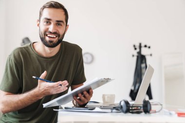 Kameraya bakıp elinde pano tutan gülümseyen yakışıklı bir adam.