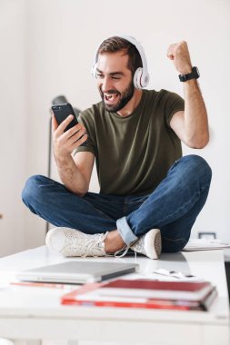 Kulaklıkla müzik dinleyen ve cep telefonu kullanan genç bir adamın görüntüsü
