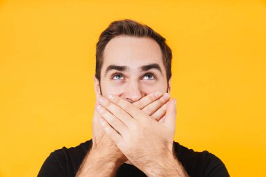 Ağzını kapatıp sana bakan tişörtlü heyecanlı bir adam resmi.