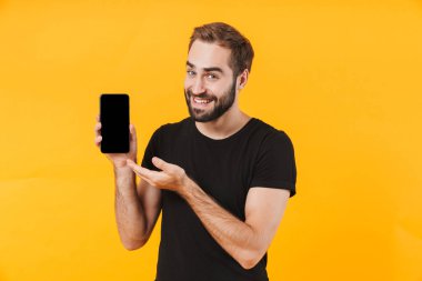 Tişört giyen, gülümseyen ve cep telefonu tutan yakışıklı bir adam.