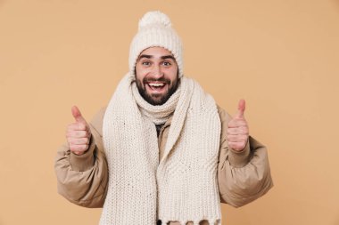 Kışlık giysiler içinde gülümseyen ve baş parmak işareti yapan genç bir adam.