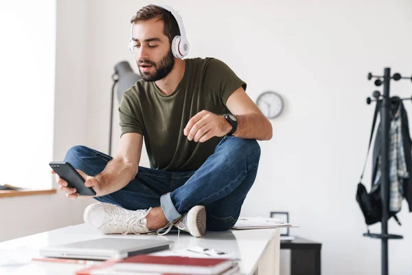 Image of calm man listening music with headphones and using cellphone