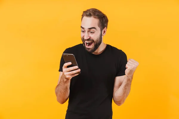 Obraz zdumionego mężczyzny noszącego t-shirt radującego się i trzymającego sm — Zdjęcie stockowe