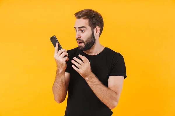 Obraz zdenerwowanego mężczyzny noszącego koszulkę trzymającą i patrzącego na smartpa — Zdjęcie stockowe
