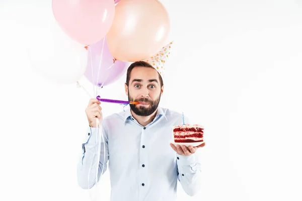 Imagen del joven soplando cuerno de fiesta y sosteniendo pastel de cumpleaños — Foto de Stock