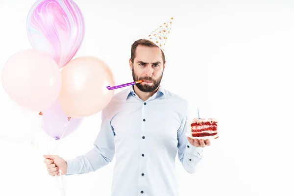 Imagem de homem sério soprando chifre de festa e segurando bolo de aniversário — Fotografia de Stock