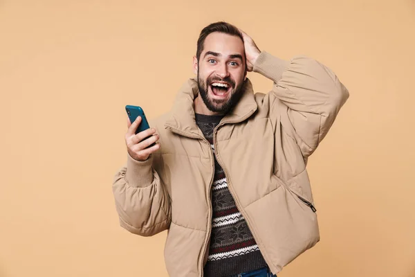 Imagen del hombre excitado en chaqueta de invierno sonriendo y sosteniendo smartp — Foto de Stock