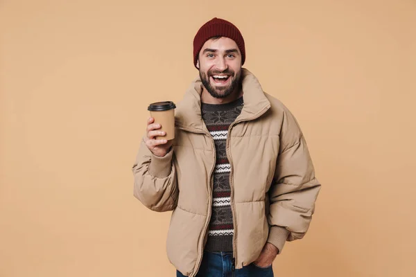 Image of young man in winter jacket and hat smiling while drinki — 스톡 사진