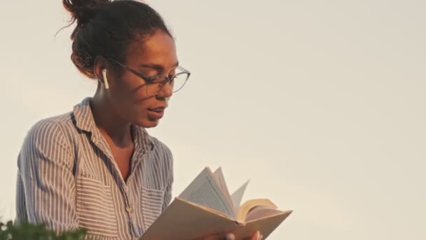 Sorrindo Mulher Africana Bonita Óculos Fones Ouvido Leitura Livro Olhando — Vídeo de Stock