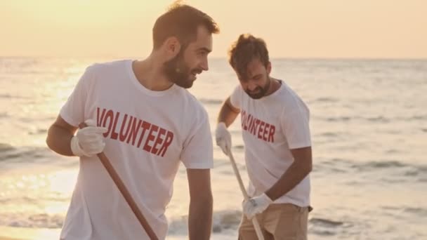 年轻英俊的志愿者正在用耙把海滩上的垃圾清理干净 — 图库视频影像