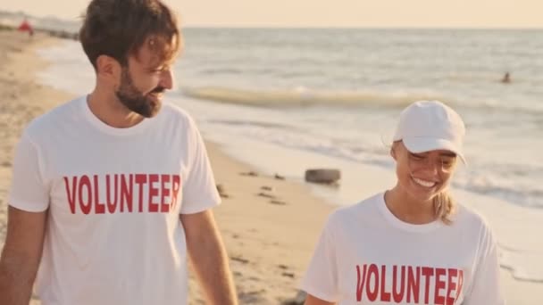 年轻的志愿者们手牵着手在海滨散步 一边用垃圾清理海滩 一边微笑着 — 图库视频影像