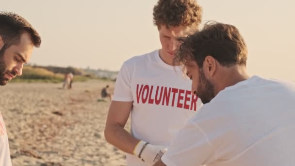 Красиві Молоді Чоловіки Добровольці Прибирають Пляж Пластику Сміттєвими Пакетами Узбережжі — стокове відео