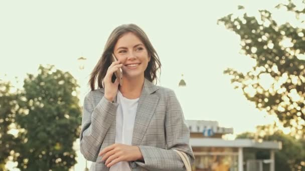 Una Chica Guapa Sonriente Está Teniendo Una Llamada Telefónica Mientras — Vídeos de Stock