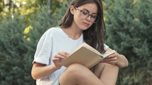 Charmante Jeune Fille Portant Des Lunettes Lit Livre Puis Regarde — Video