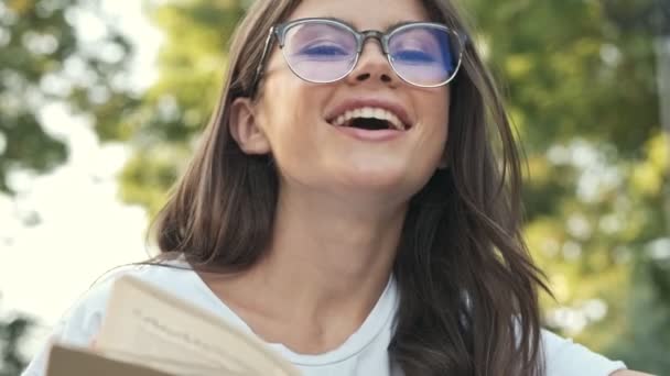 Jovencita Alegre Con Gafas Ríe Mientras Lee Libro Fuera Parque — Vídeo de stock