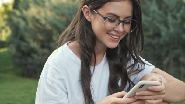 Jovem Feliz Positivo Usando Óculos Está Usando Smartphone Fora Parque — Vídeo de Stock