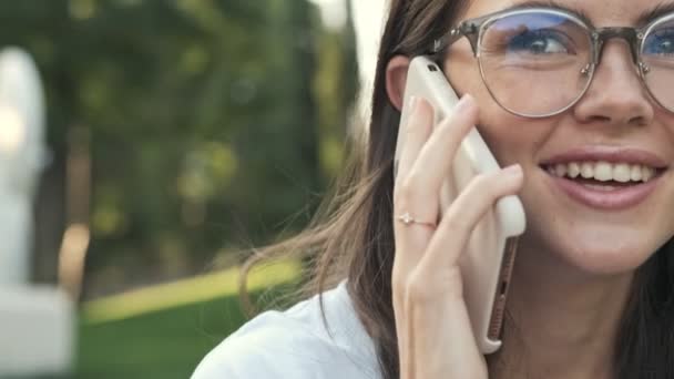 Hermosa Chica Con Gafas Sonríe Mientras Recibe Una Llamada Telefónica — Vídeos de Stock