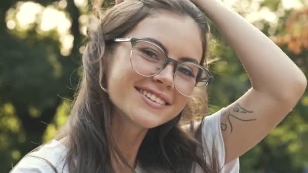 Linda Chica Sonriente Con Gafas Está Tocando Cabello Mientras Mira — Vídeo de stock