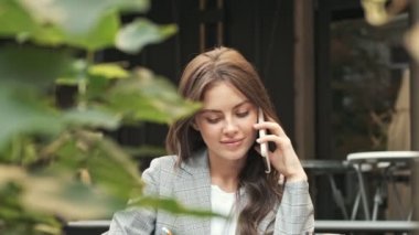 Güzel genç bir kadın kafede telefonla konuşurken not mu alıyor? Açık havada.