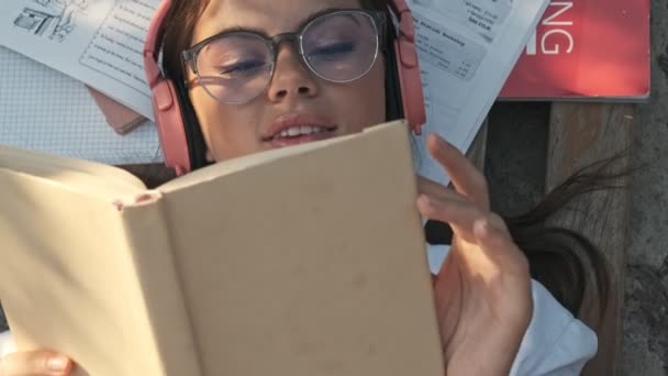 Horní Pohled Usměvavé Dívky Nosí Brýle Bezdrátové Sluchátka Leží Knihami — Stock video
