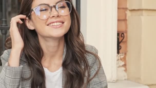 Positive Smiling Girl Wearing Glasses Correcting Her Hairstyle While Sitting — ストック動画