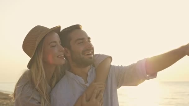 一对年轻貌美的夫妇在海滩拥抱对方的同时 也在欣赏美丽的风景 — 图库视频影像