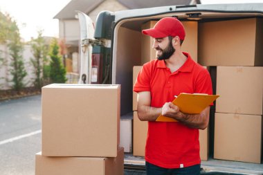 Paket kutuların yanında duran gülümseyen teslimatçı adam resmi