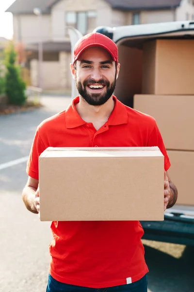 Immagine di giovane uomo sorridente consegna in piedi con la scatola dei pacchi — Foto Stock