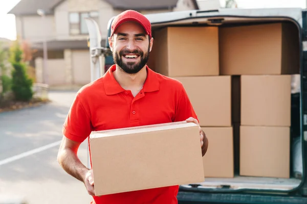 Image of smiling young delivery man standing with parcel box — Stock Photo, Image