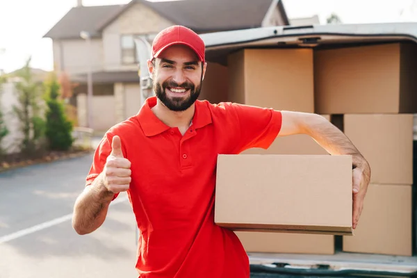 Image of delivery man standing with parcel box and showing thumb up — Stock Photo, Image