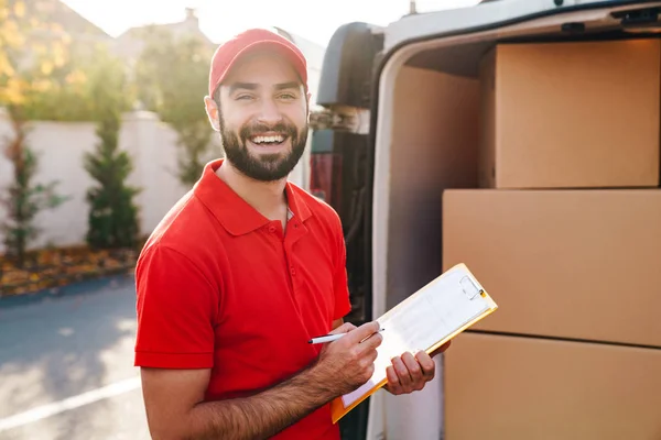 Image of smiling delivery man holding clipboard and writing