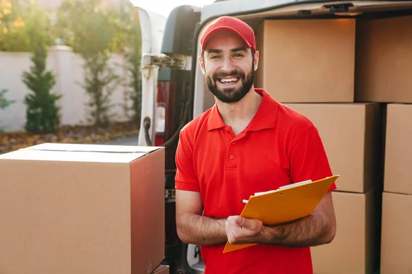 Image of delivery man holding clipboard while standing with boxes