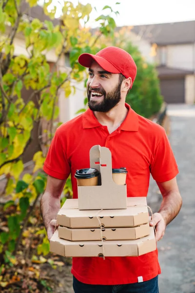 Image of smiling young delivery man holding pizza boxes and coffee — Stock Photo, Image