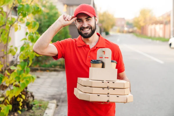 Imagem do jovem homem de entrega sorrindo segurando caixas de pizza e café — Fotografia de Stock