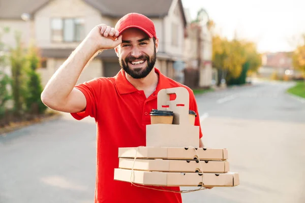 Pizza kutuları ve kahve taşıyan neşeli bir teslimatçı. — Stok fotoğraf