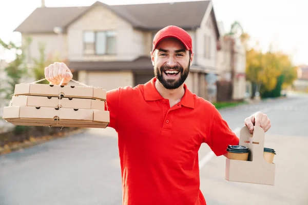 Imagem do jovem homem de entrega alegre segurando caixas de pizza e café — Fotografia de Stock