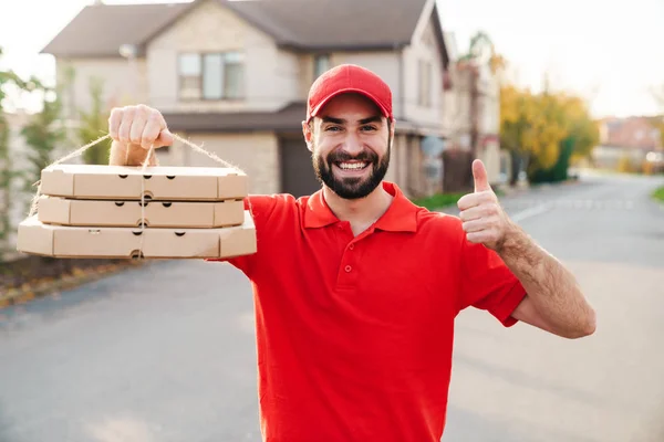 Bild eines freudigen Zustellers, der Pizzakartons hält und den Daumen nach oben zeigt — Stockfoto