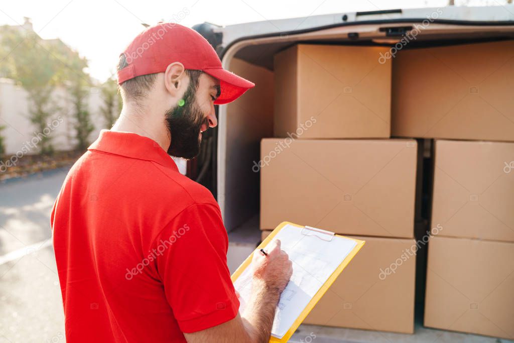 Image of young delivery man holding clipboard and writing