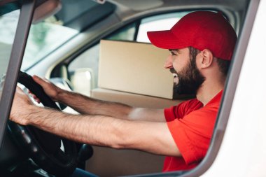 Gülümseyen ve şoförlük yapan mutlu sakallı teslimatçı.