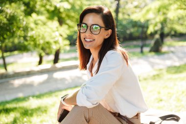 Mutlu ve çekici genç bir kadın bankta dinleniyor.