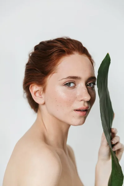 Joven pelirroja posando aislada sobre fondo blanco de pared con hojas de flores verdes . — Foto de Stock