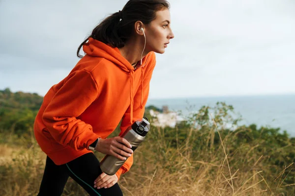 Photo of young athletic woman using earphones and holding water bottle — Stock Photo, Image