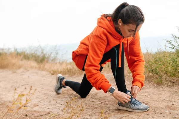 Foto de una linda atlética usando auriculares y atándose los cordones de los zapatos — Foto de Stock