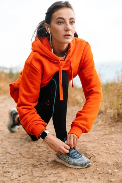 Photo of nice athletic woman using earphones and tying her shoelaces — Stock Photo, Image