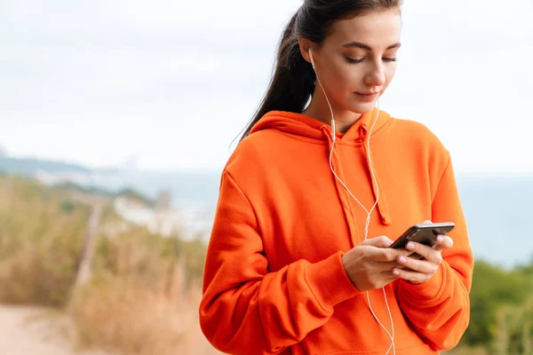 Foto de bela mulher morena usando fones de ouvido e celular — Fotografia de Stock