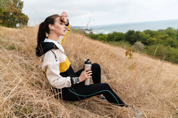 Foto av trött brunett kvinna sjunga hörlurar och dricksvatten — Stockfoto